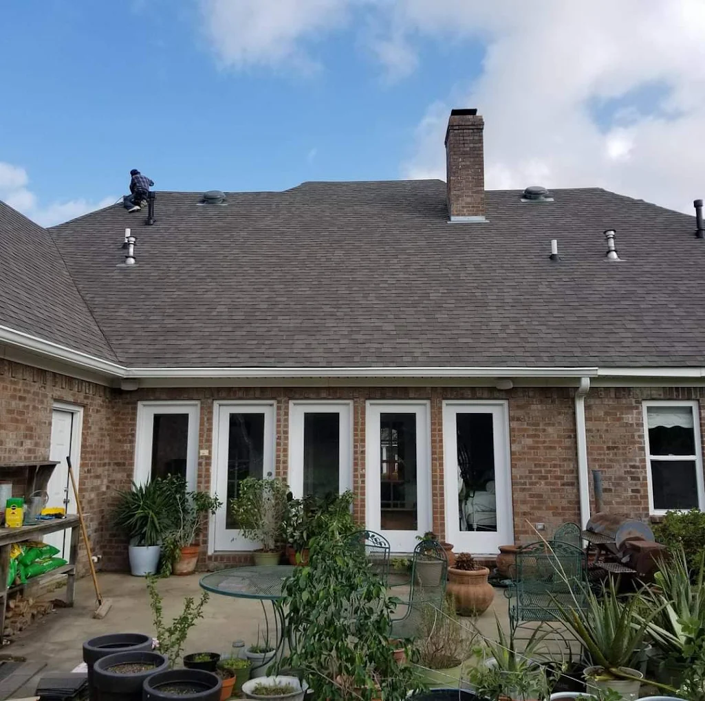 Roofer working on the rear roof of a large brick home